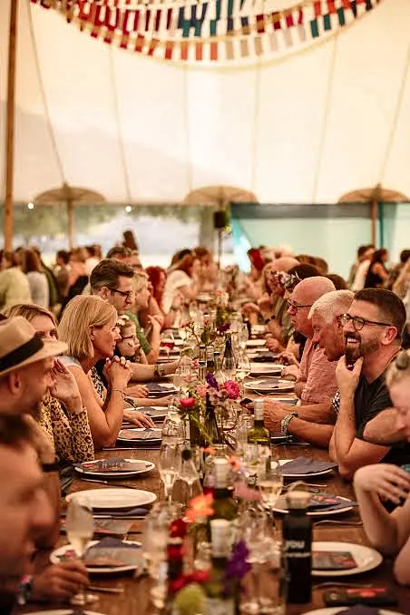 Guests at long tables with wine under a festival marquee