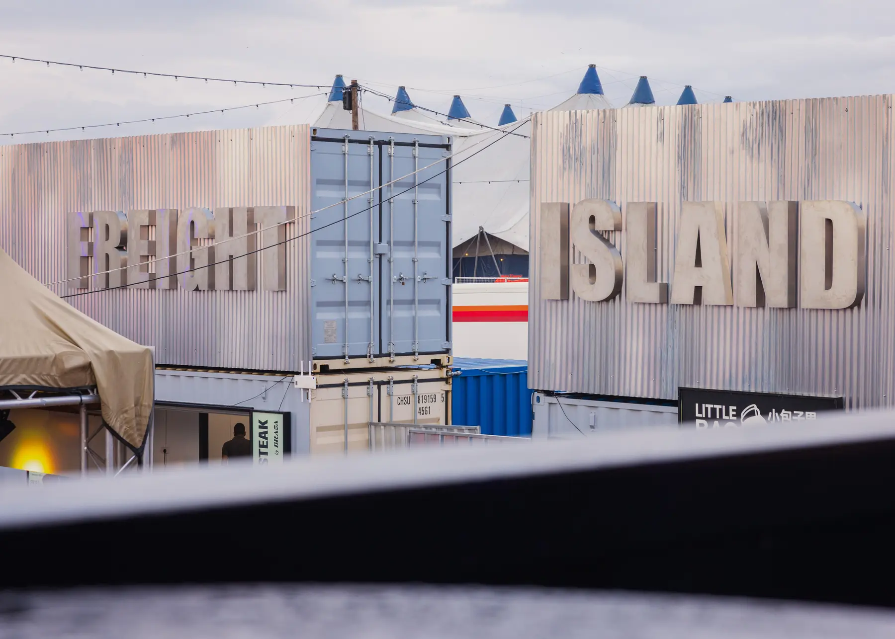 Container-built festival bar village with big-top tents behind