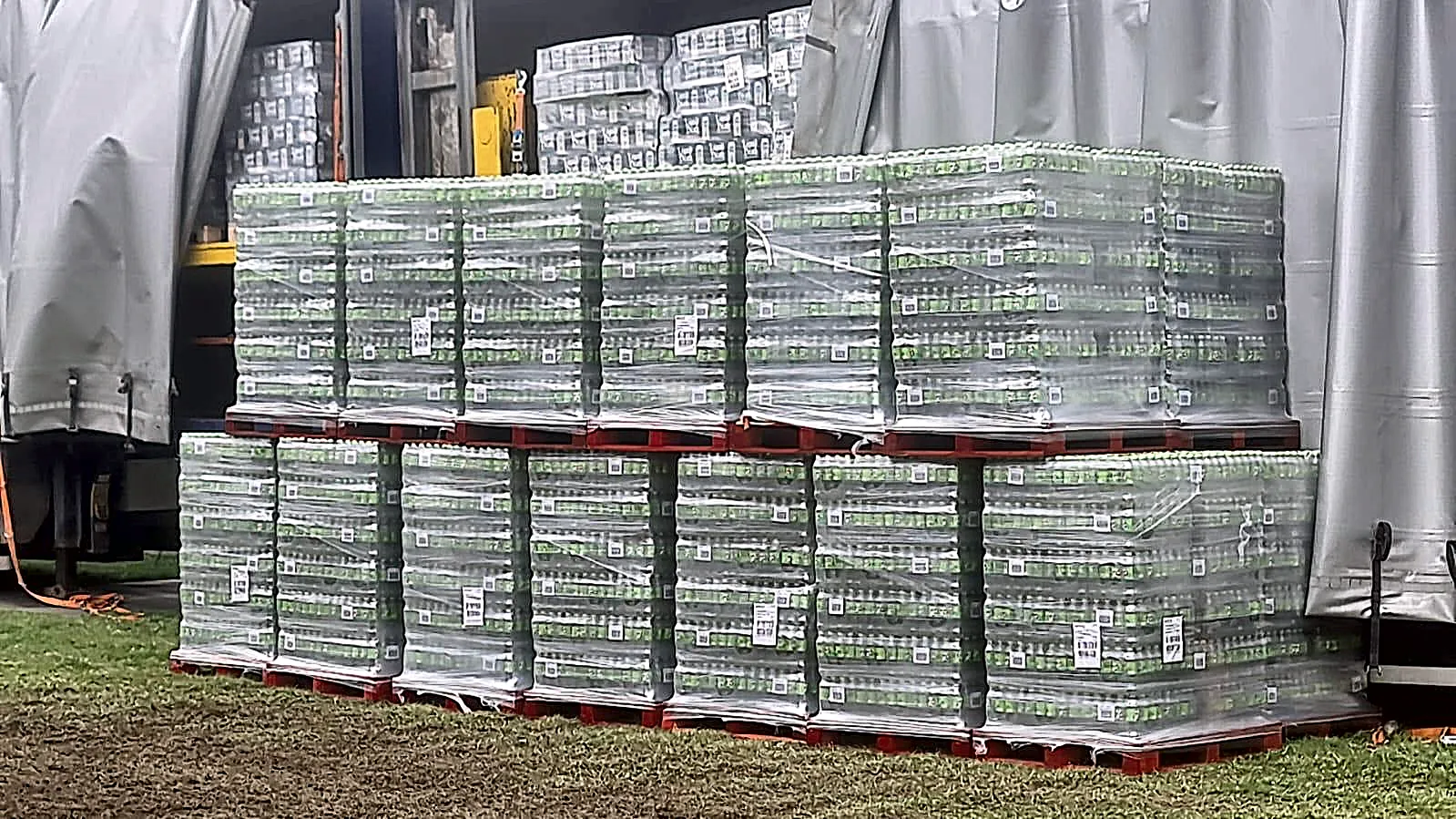Stacked pallets of bottled drinks in front of an open curtain-sider