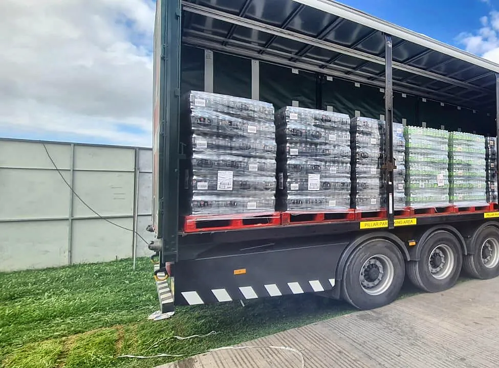 Curtain-side trailer opened on site, loaded with pallets of soft drinks and water