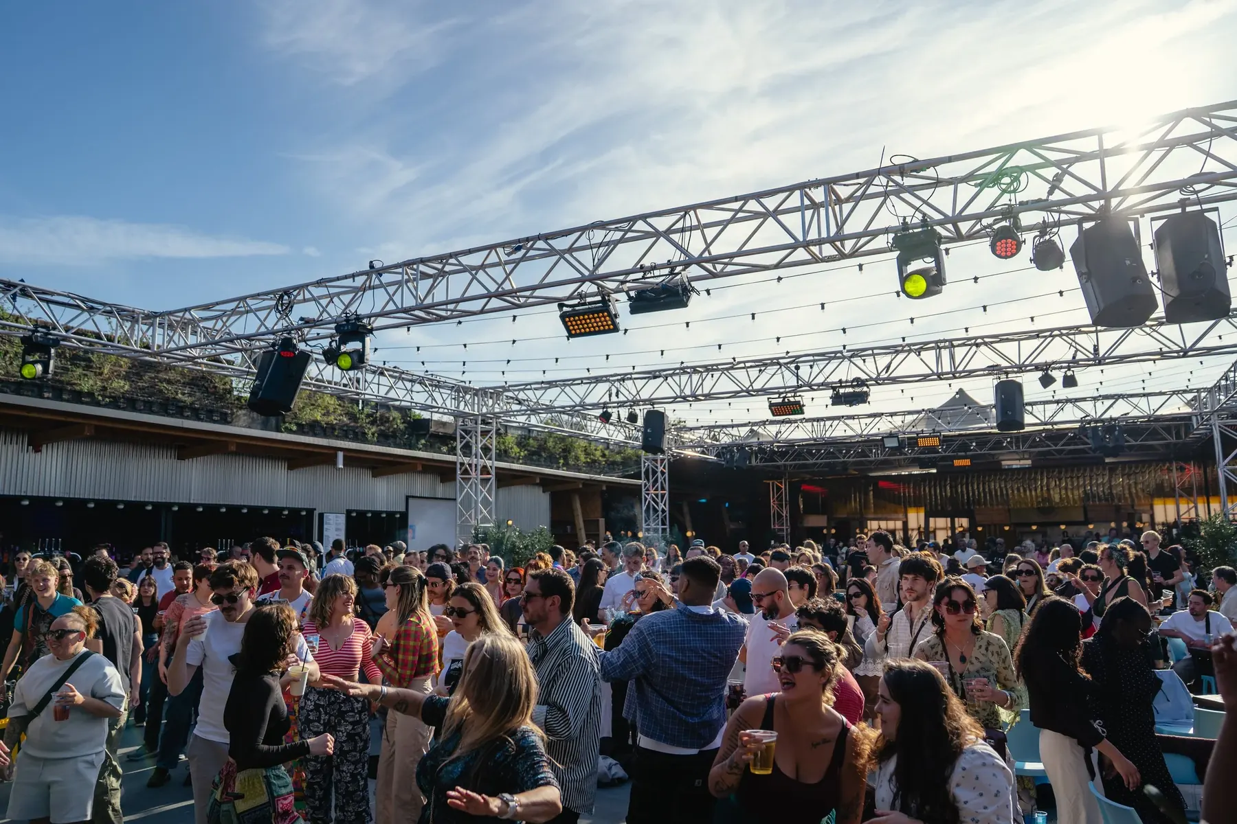 Crowd on an outdoor venue terrace under a lighting rig
